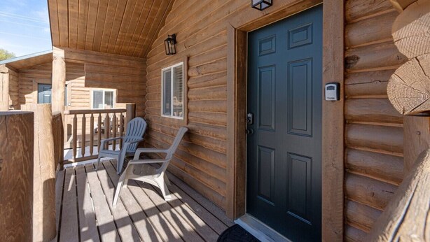Une cabane en bois dotée d’un porche, de deux fauteuils Adirondack, d’une porte bleu foncé et d’une petite fenêtre avec des volets.