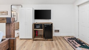 Una habitación compacta con televisor de pantalla plana en la pared, un mueble de madera con microondas y un refrigerador pequeño.
