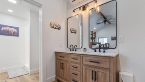 Un baño con armarios de madera, una encimera blanca y dos espejos con luces.