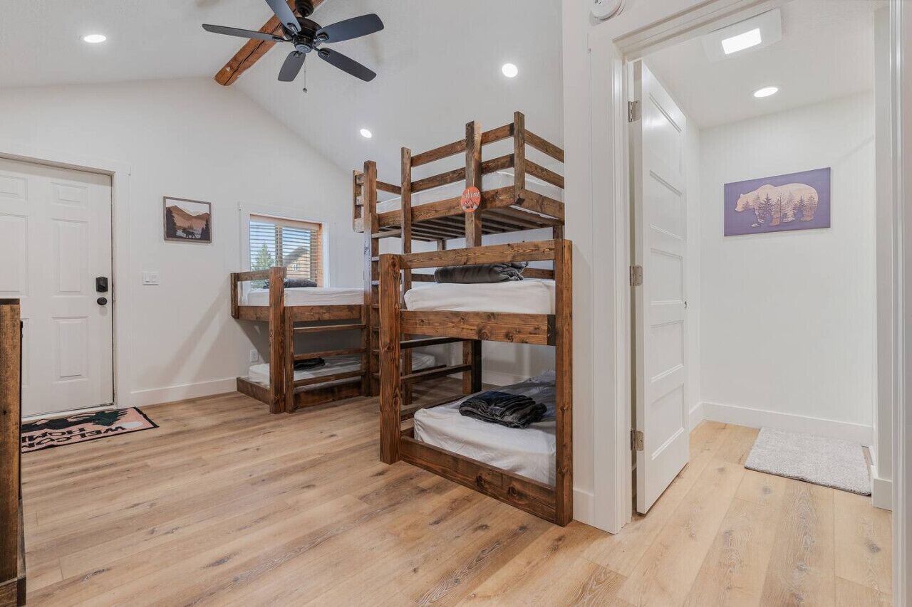 A room with a bunk bed, wooden flooring, a ceiling fan, and a door with a doormat.