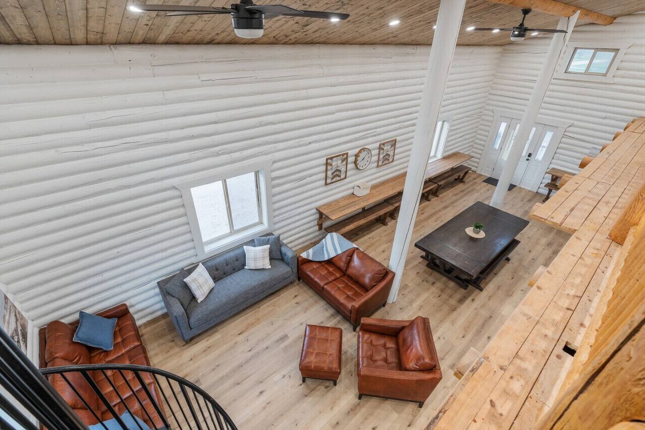 A spacious interior with a loft-style layout, featuring a staircase, multiple seating areas, and a large window providing natural light.
