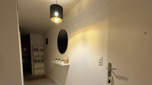 A hallway with a light fixture, a door, a black rug, and a shelf with small plants. - New apartment 5 minutes from Rouen's historic center - breathtaking view. (Rouen)