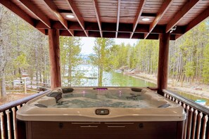 Un bain à remous avec une terrasse en bois et une vue sur une rivière et une forêt.