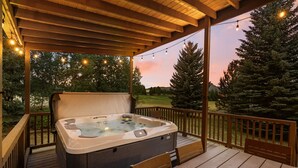 Un jacuzzi en una terraza de madera con vista a árboles y al atardecer.