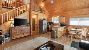 A spacious cabin with a wooden interior, a dining area with wooden chairs, a kitchen with stainless steel appliances, and a TV on a wooden cabinet.