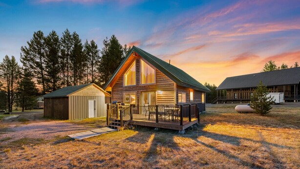 A log cabin with a deck, surrounded by a forest.