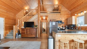 A wooden cabin interior with a staircase, kitchen, and bar area.