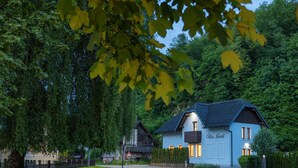 En tvåvåningsbyggnad med ett mörkt tak och ljusa väggar, märkt med namnet ”Villa Grad”, omgiven av frodig grönska och ett trästaket.