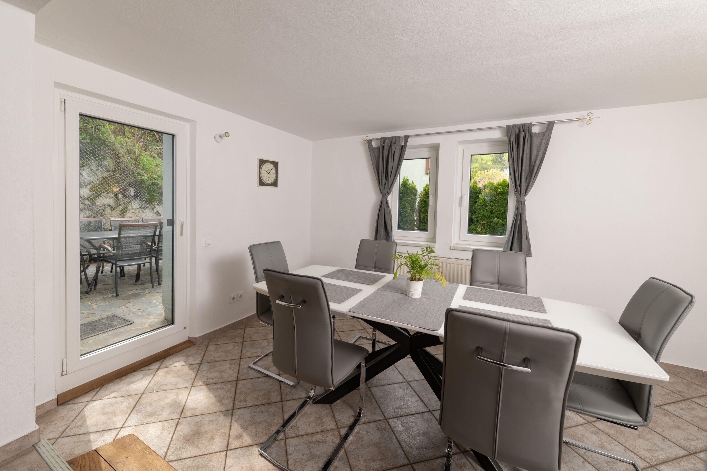 A dining area with a table and chairs, a potted plant, and a view of the outdoors through a glass door.