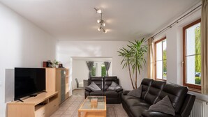 Ett modernt vardagsrum med en platt-TV, lädersoffor, ett soffbord i glas och ett stort fönster med gardiner.
