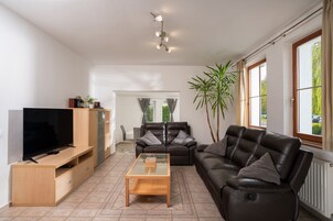 Una sala de estar moderna con un televisor de pantalla plana, sofás de cuero, una mesa de centro de vidrio y un ventanal con cortinas.
