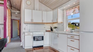 A modern kitchen with white cabinets, a built-in oven, and a window with a view of houses. - 5 Star Holiday Home in Lokken (Lokken)