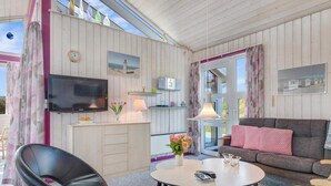 A modern living room with a flat-screen TV, a sofa, a dining table, and a chair. - 5 Star Holiday Home in Lokken (Lokken)
