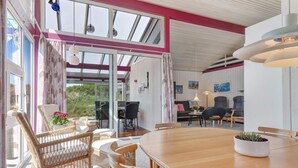 A spacious room with a large wooden dining table, wicker chairs, and a view through a glass door to an outdoor area. - 5 Star Holiday Home in Lokken (Lokken)