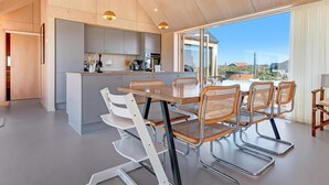 A modern kitchen with a central island, a dining area with a table and chairs, and large windows offering a view of the outdoors. - 5 Star Holiday Home in Lokken (Lokken)