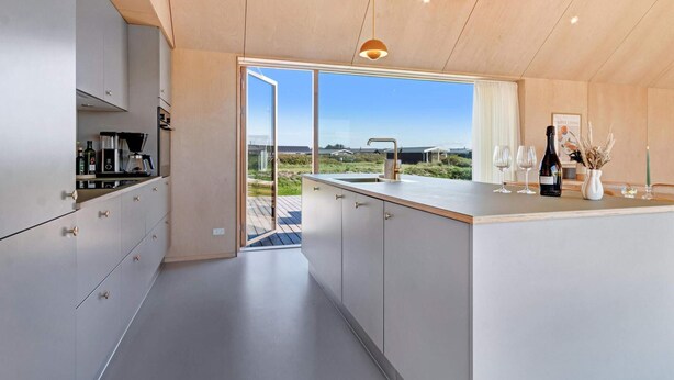 A modern kitchen with a large island, built-in appliances, and a view of the countryside. - 5 Star Holiday Home in Lokken (Lokken)