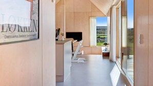 A modern interior with a minimalist design, featuring a large window with a view of the countryside, a flat-screen TV, and a dining area with a table and chairs. - 5 Star Holiday Home in Lokken (Lokken)