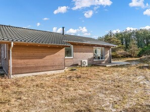 Une maison en bois d’un seul étage, avec un toit en tuiles, un petit porche et un appareil de climatisation visible.