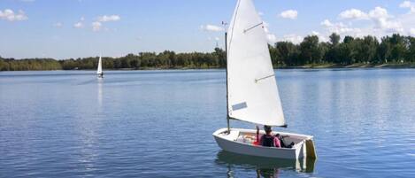 A calm lake with a sailboat in the foreground and another in the distance.