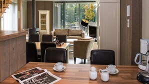A modern living room with a wooden dining table, chairs, a sofa, and a TV. - Elegant Villa for 8 Guests (Froidchapelle)