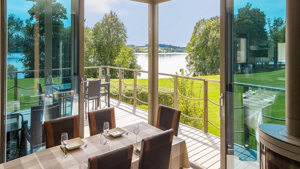 Un espace repas offrant une vue sur un lac et la verdure environnante.