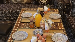 Une table à manger dressée dans un style décoratif marocain traditionnel, avec des nappes à motifs, des assiettes décorées et une variété de plats.