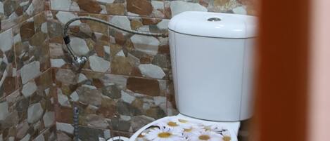 A bathroom with a mosaic tile wall, a toilet with a floral seat cover, and a plunger on the floor.