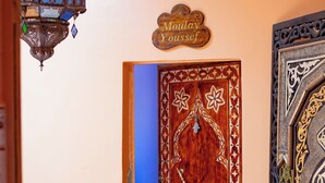 Un intérieur marocain traditionnel, avec une porte en bois, une lanterne suspendue et un élément décoratif en métal au-dessus de la porte.