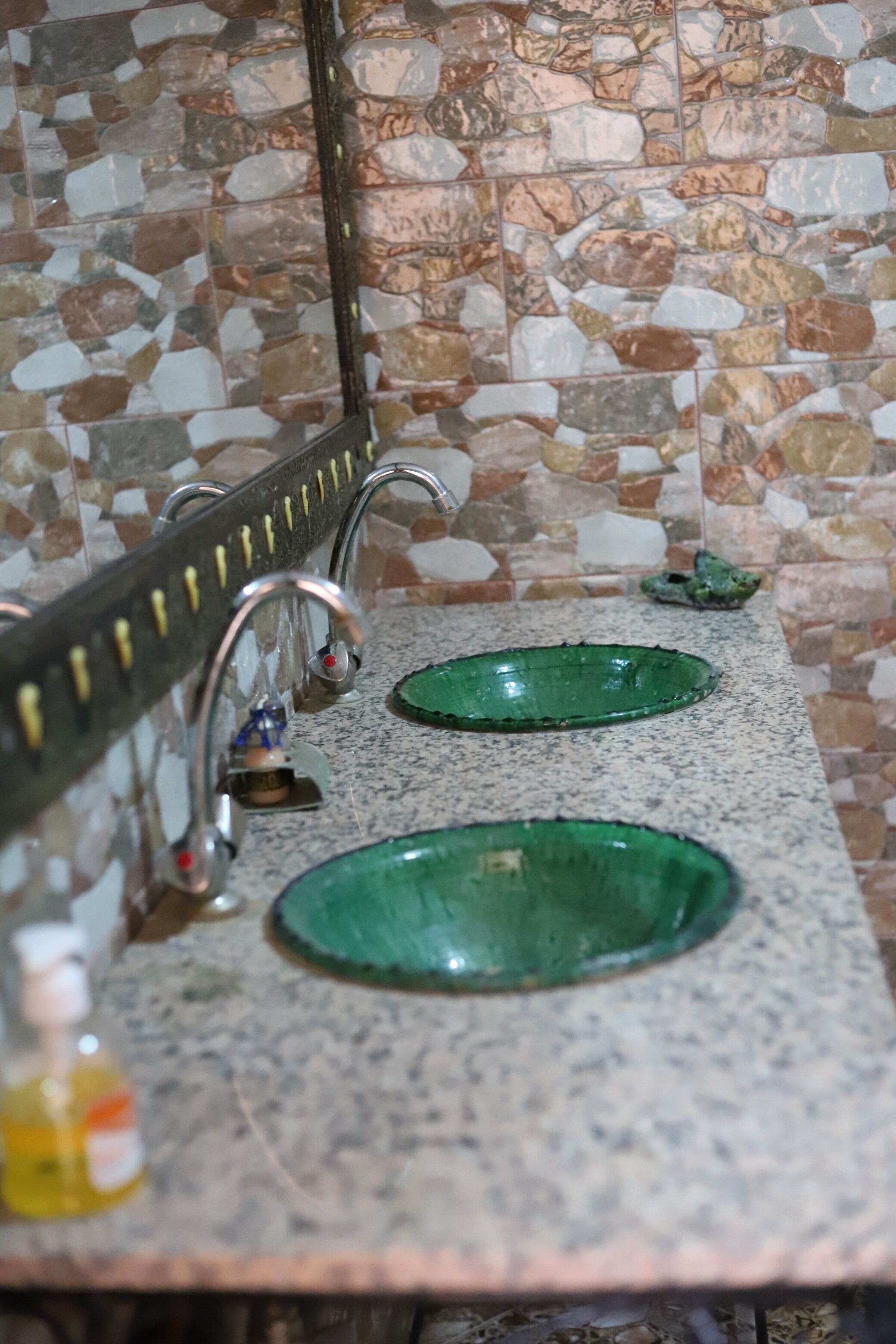 A bathroom with two green glass sinks, a mirror, and a soap dispenser.