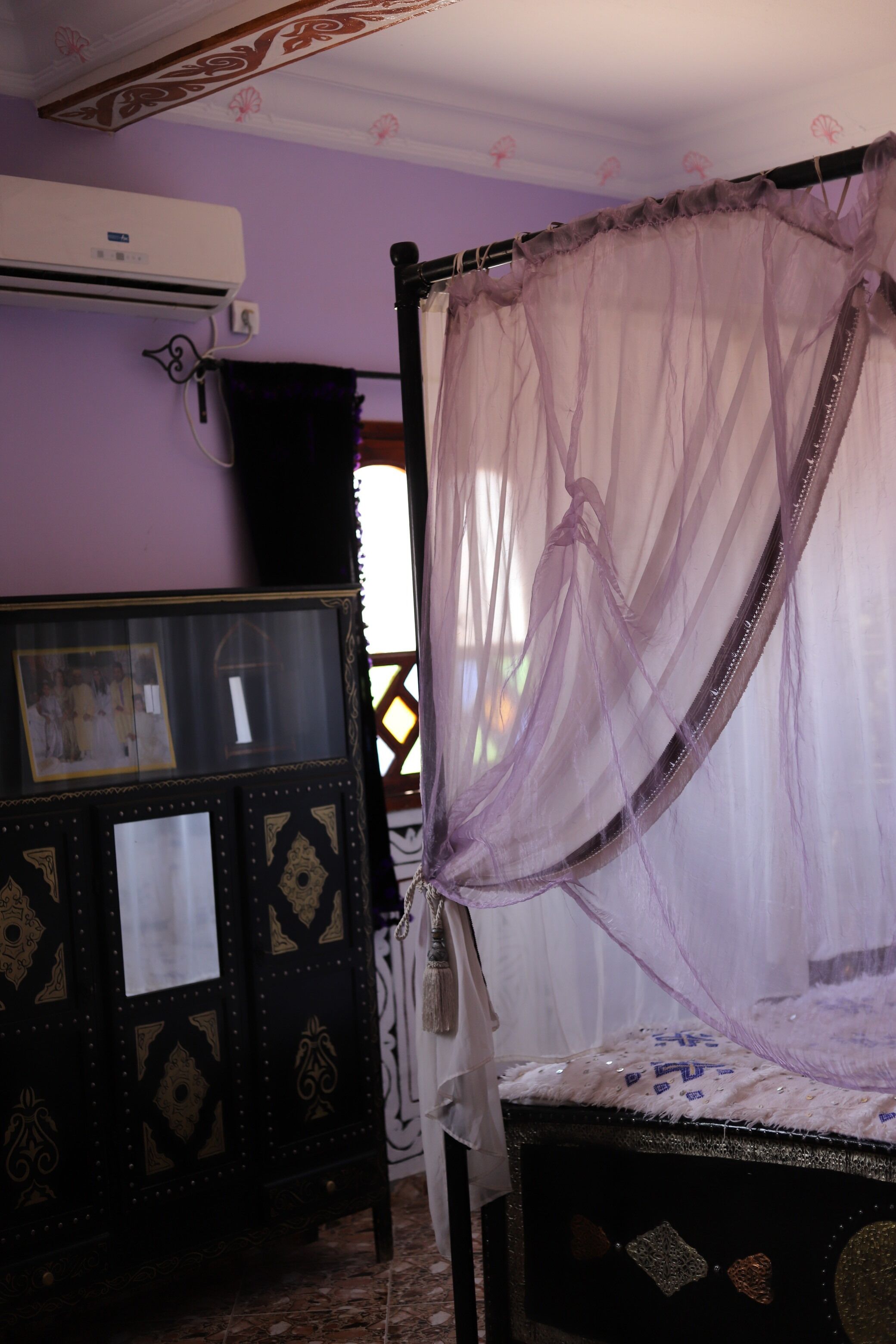Una habitación con una cama bajo una dosel, un aparador decorativo y un equipo de aire acondicionado.