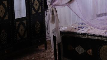 Una habitación con una cama bajo una dosel, un aparador decorativo y un equipo de aire acondicionado.