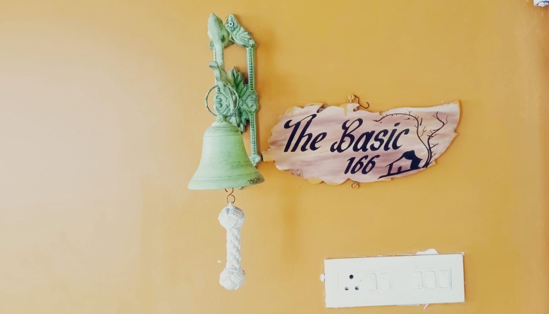 A wall with a green decorative bell, a sign reading "The Basic 166", and a power outlet.
