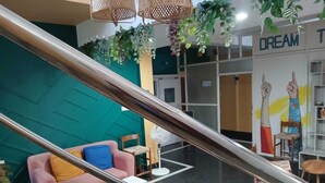 A modern interior with a staircase, a teal accent wall, a pink sofa, and a mural with raised hands. - The Basic (Bhubaneshwar)