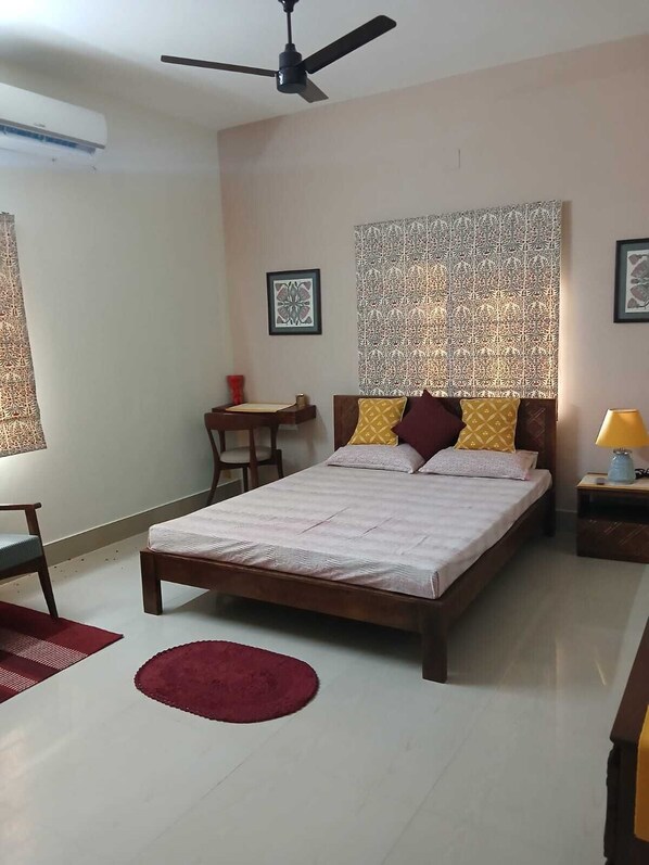 A bedroom with a bed, a ceiling fan, a patterned wall, and a small table with a chair.