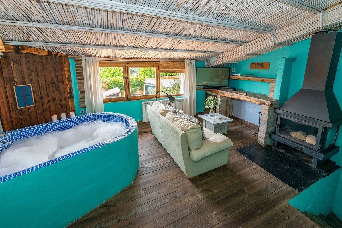Una habitación acogedora con jacuzzi, sofá, chimenea y vistas al exterior.