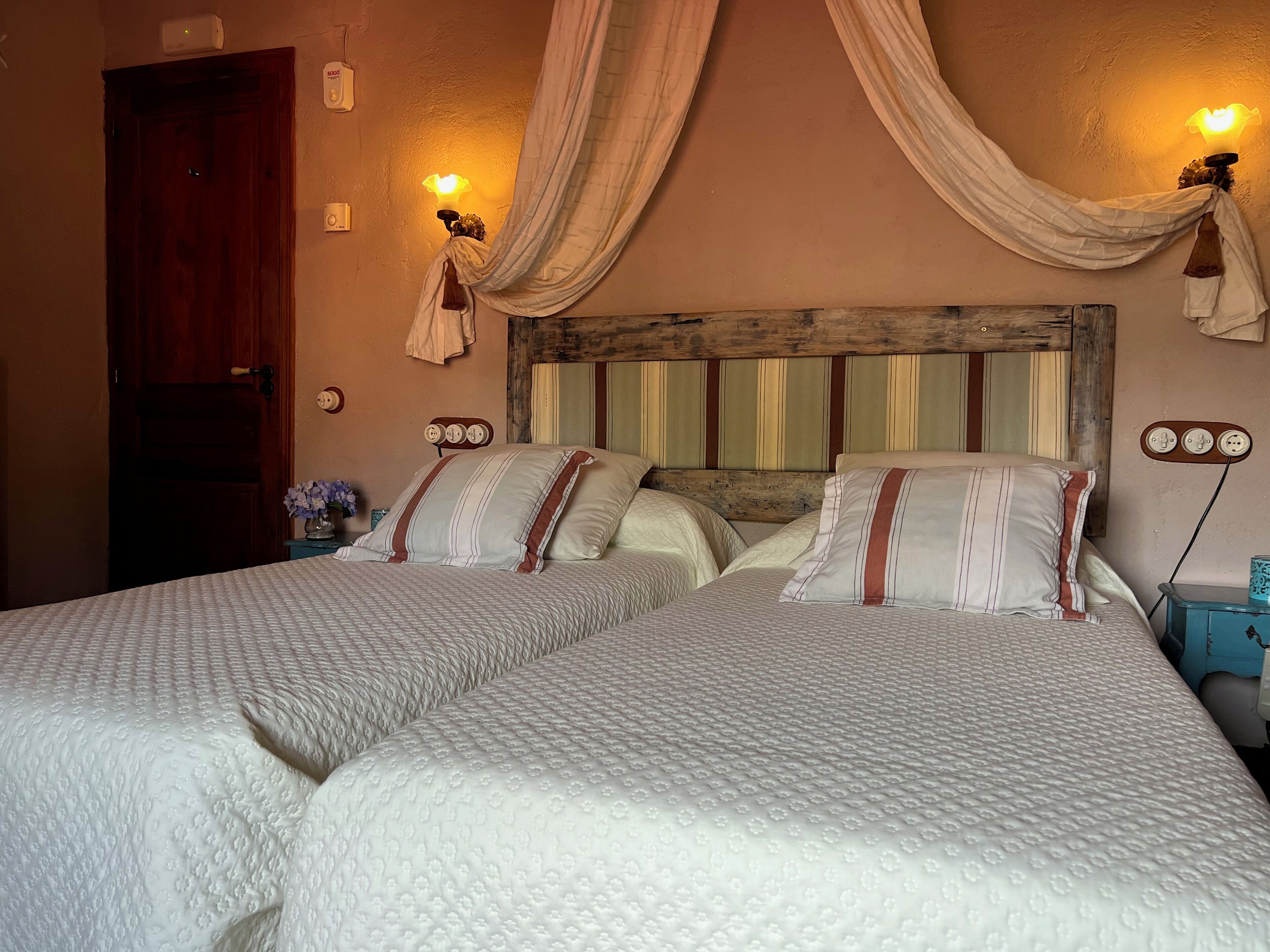 A double bed with a striped headboard, two bedside tables with lamps, and a wooden door.