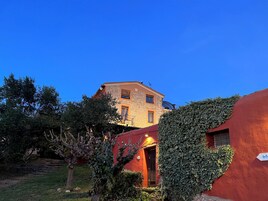 Um edifício de pedra com fachada vermelha, rodeado por vegetação e árvores.