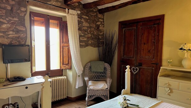Quarto com parede de pedra, porta de madeira e cama com colcha branca.