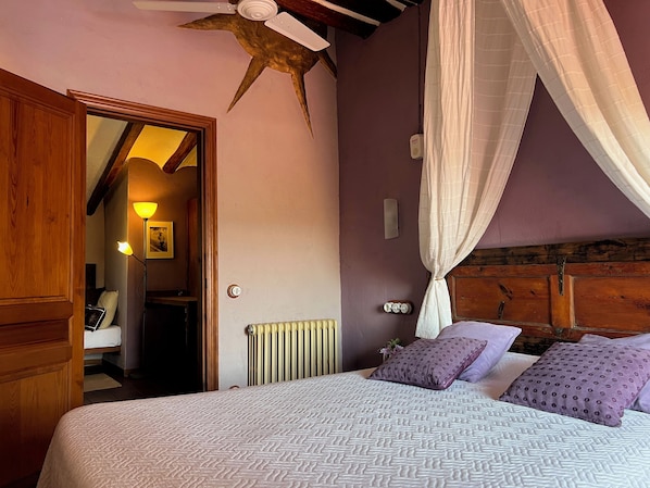 A bedroom with a bed, purple pillows, a ceiling fan, and a window with curtains. - Les Vinyes Hotel Boutique & Spa (Montferri)