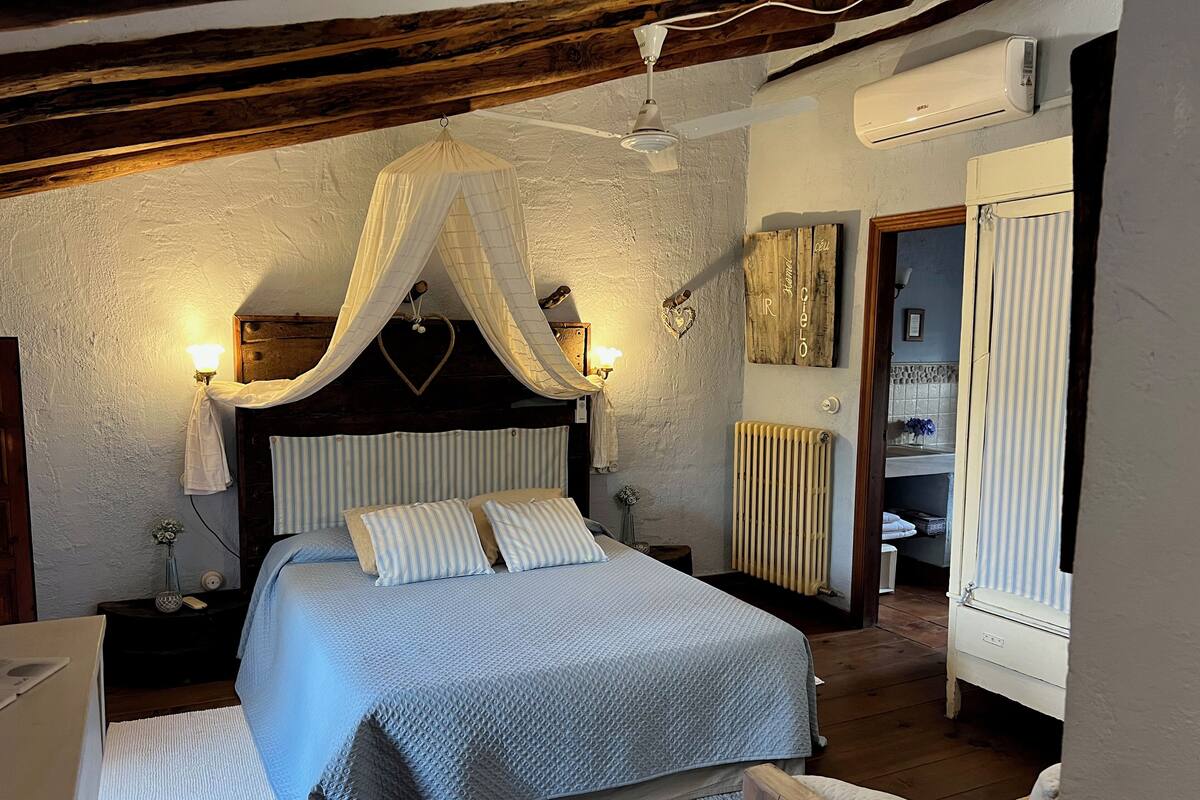 Un dormitorio con cama con dosel, lámparas de noche, radiador y techo de madera.