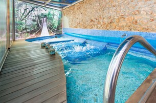 Uma área de spa com um deck de madeira, uma parede de pedra e uma vista para uma ponte suspensa ao fundo.