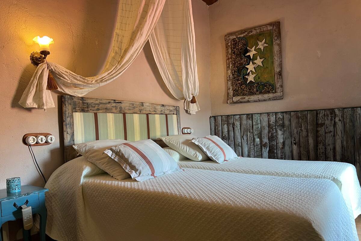 Una cama doble con cabecera de madera, dos mesitas de noche, una lámpara de pared y un cuadro decorativo.