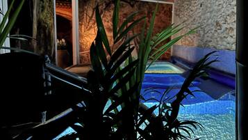 A room with a stone wall, a blue pool, and a seating area.