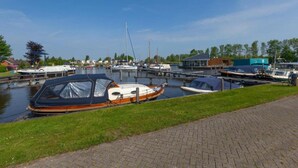 Een gracht met aangemeerde boten, een grasveld en een verhard pad.