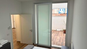 Een slaapkamer met een bed, een nachtkastje, een schuifdeur naar een balkon en een kleine potplant.