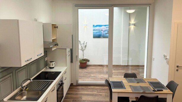 Een compacte keuken met een modern design, inclusief een ingebouwde oven en een koffieapparaat. Er is een zithoek met een tafel en stoelen, en een schuifdeur naar een balkon met uitzicht op zee.