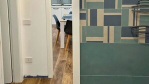 Een gang met een betegelde muur, een houten vloer en een deur die uitkomt in een eetgedeelte.