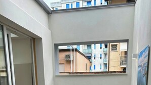 Een balkon met uitzicht op omliggende gebouwen, een bloempot en een raam.