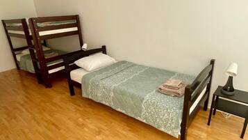 A room with a bunk bed, a single bed, a bedside table with a lamp, and a wooden floor.