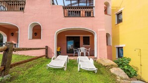 Un bâtiment à la façade rose, doté d’un balcon et d’un mur jaune. On y trouve deux fauteuils de jardin blancs et une table avec des chaises à l’extérieur.